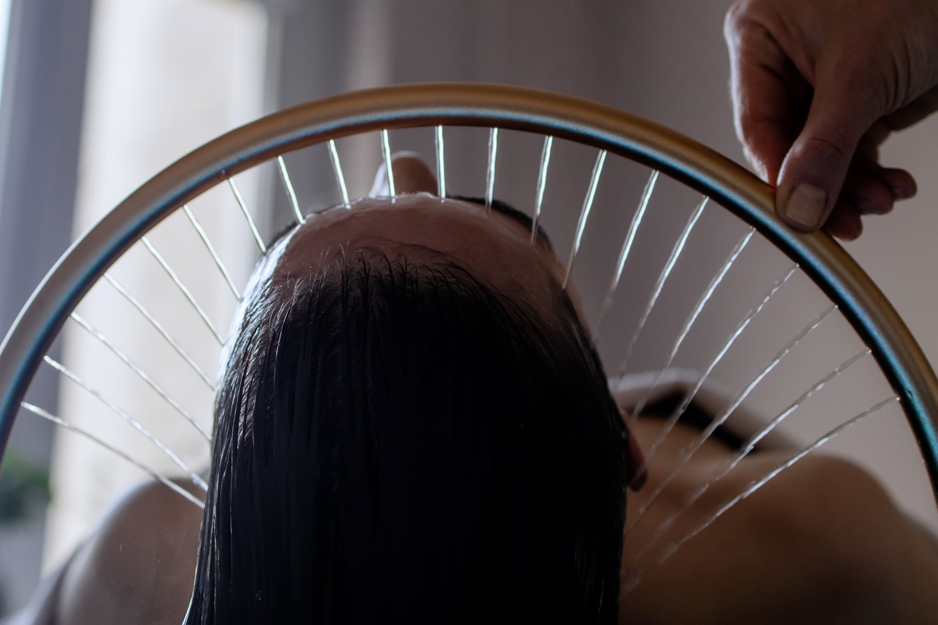 Close-up of a woman receiving a head massage during a Japanese head spa treatment with water flowing from a special hair washing tool, focusing on the scalp relaxation and beauty therapy